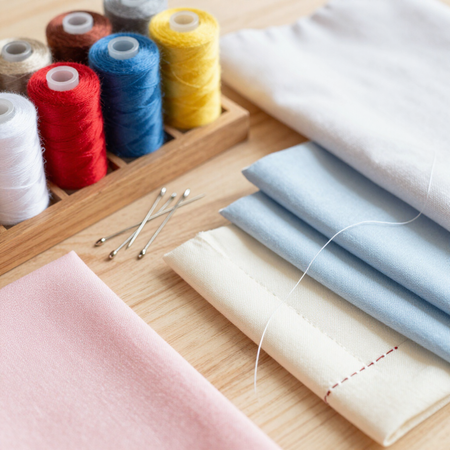 Carretes de hilo de colores, alfileres y tela doblada sobre una mesa de madera para coser.