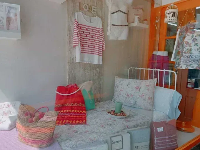 Habitación acogedora con una cama blanca, bolsos coloridos y ropa a rayas colgada en la pared.