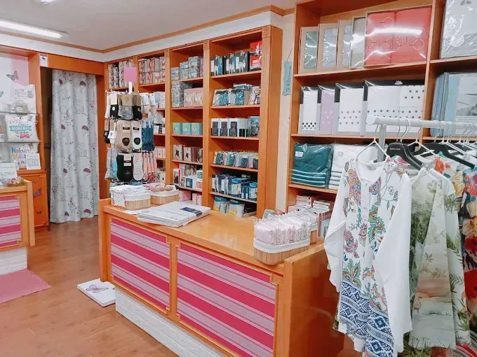 Mostrador luminoso con estantes llenos de telas dobladas, suministros y camisas estampadas colgadas en una tienda.
