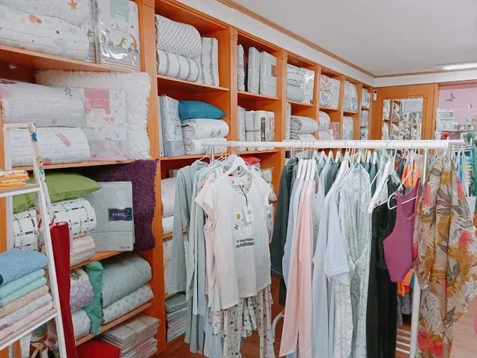 Tienda de ropa con sábanas dobladas en estantes y prendas de colores pastel colgadas en percheros.