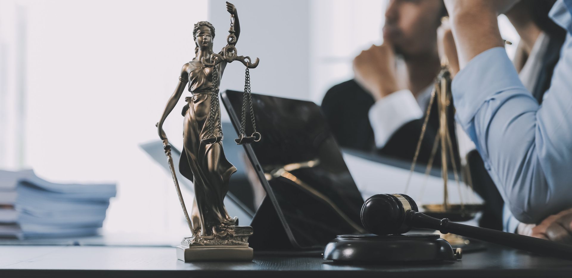 Primer plano de una reunión con una estatua de la Dama de la Justicia, un mazo y personas vestidas de negocios.
