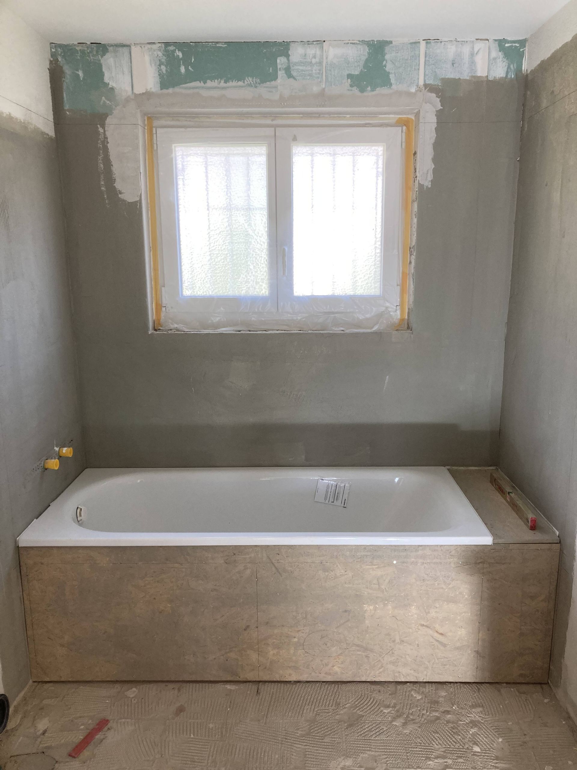 Badezimmer im Bau, mit weißer Badewanne, Fenster und grauen Wänden.