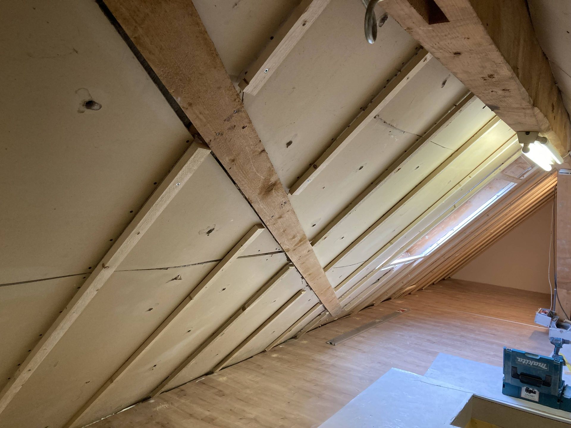 Schräge Decke mit freiliegenden Balken und weißer Verkleidung in einem Raum.