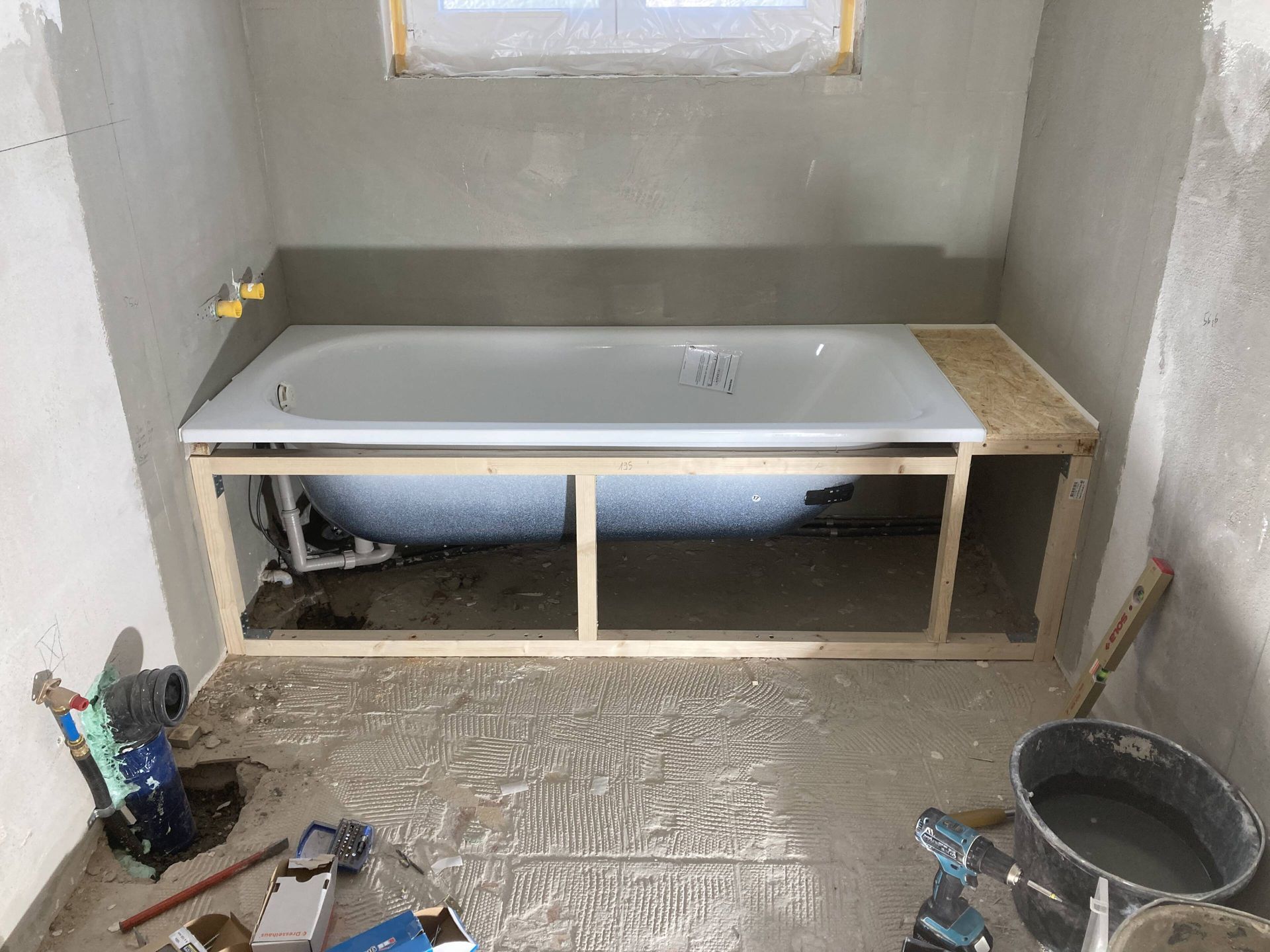 Badewanneneinbau im Badezimmer: Holzrahmen umschließt Wanne, Wände frisch verputzt.