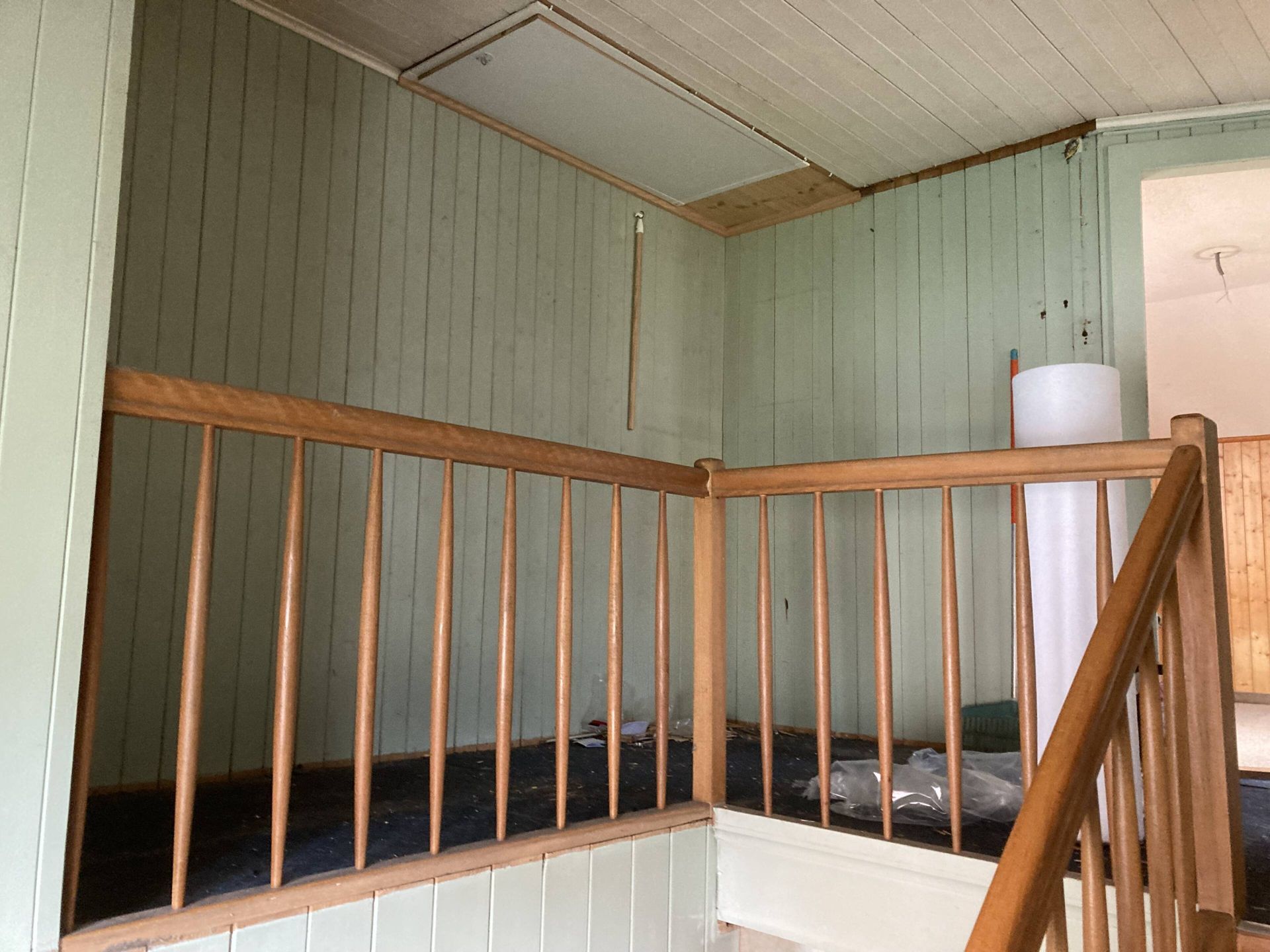 Holzgeländer in einem Raum mit grün getäfelten Wänden und einer Luke in der Decke.