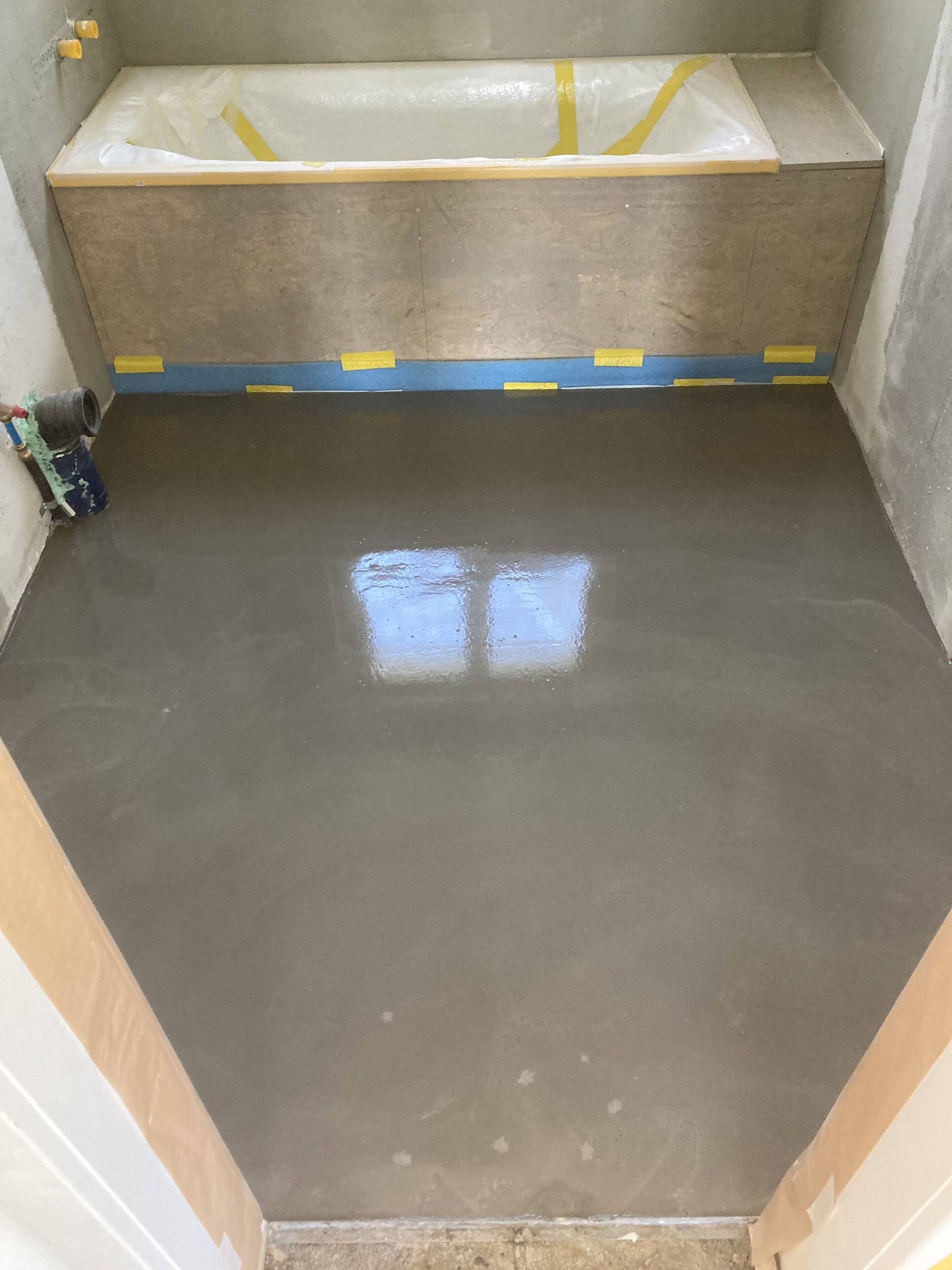 Frisch gegossener Betonboden in einem Badezimmer, im Hintergrund eine Badewanne.