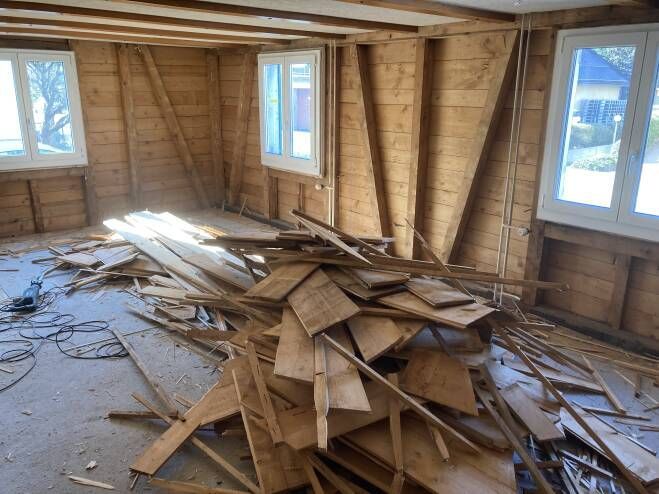 Zimmer wird renoviert, mit freiliegenden Holzwänden, Schutt auf dem Boden und den Fenstern.