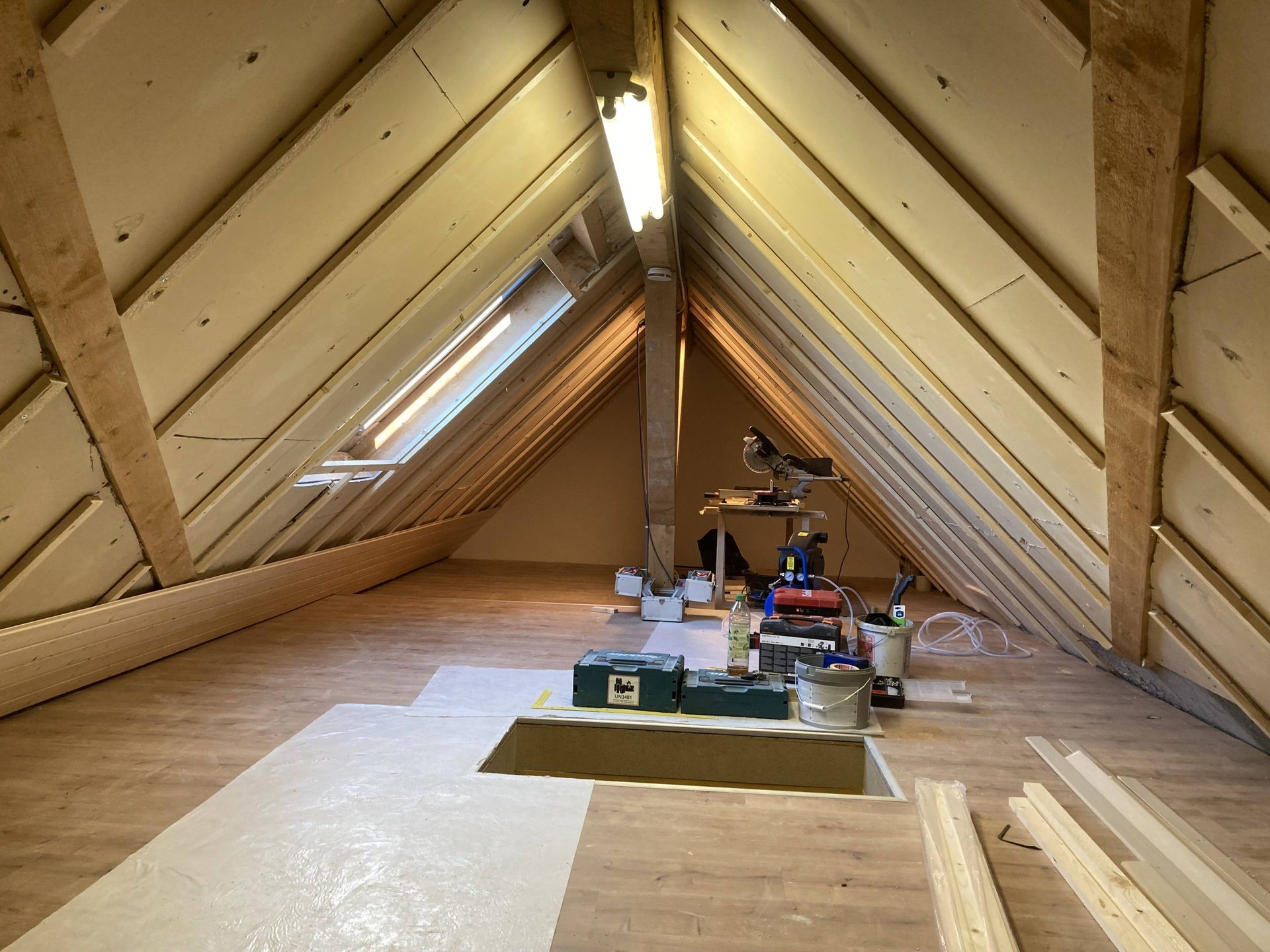 Dachbodeninnenraum mit freiliegenden Balken, Isolierung und Werkzeugen.