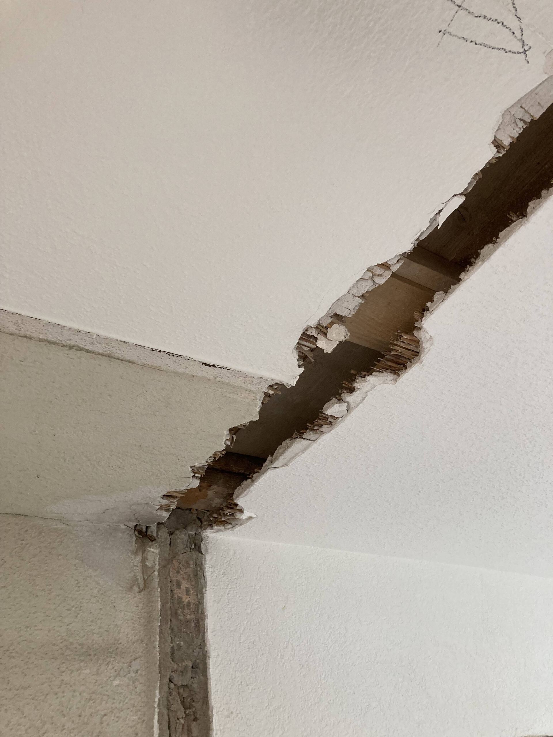 Beschädigte weiße Decke mit einem großen Riss, der die darunterliegende Struktur freilegt.