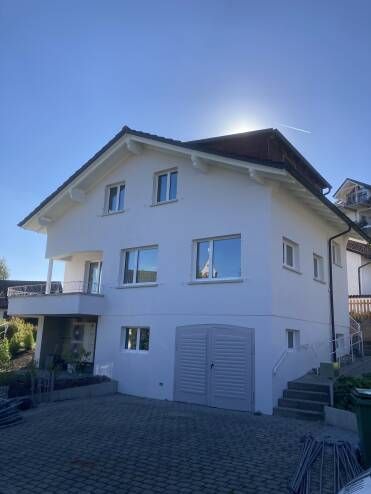 Weißes zweistöckiges Haus mit Garage und Balkon an einem sonnigen Tag.