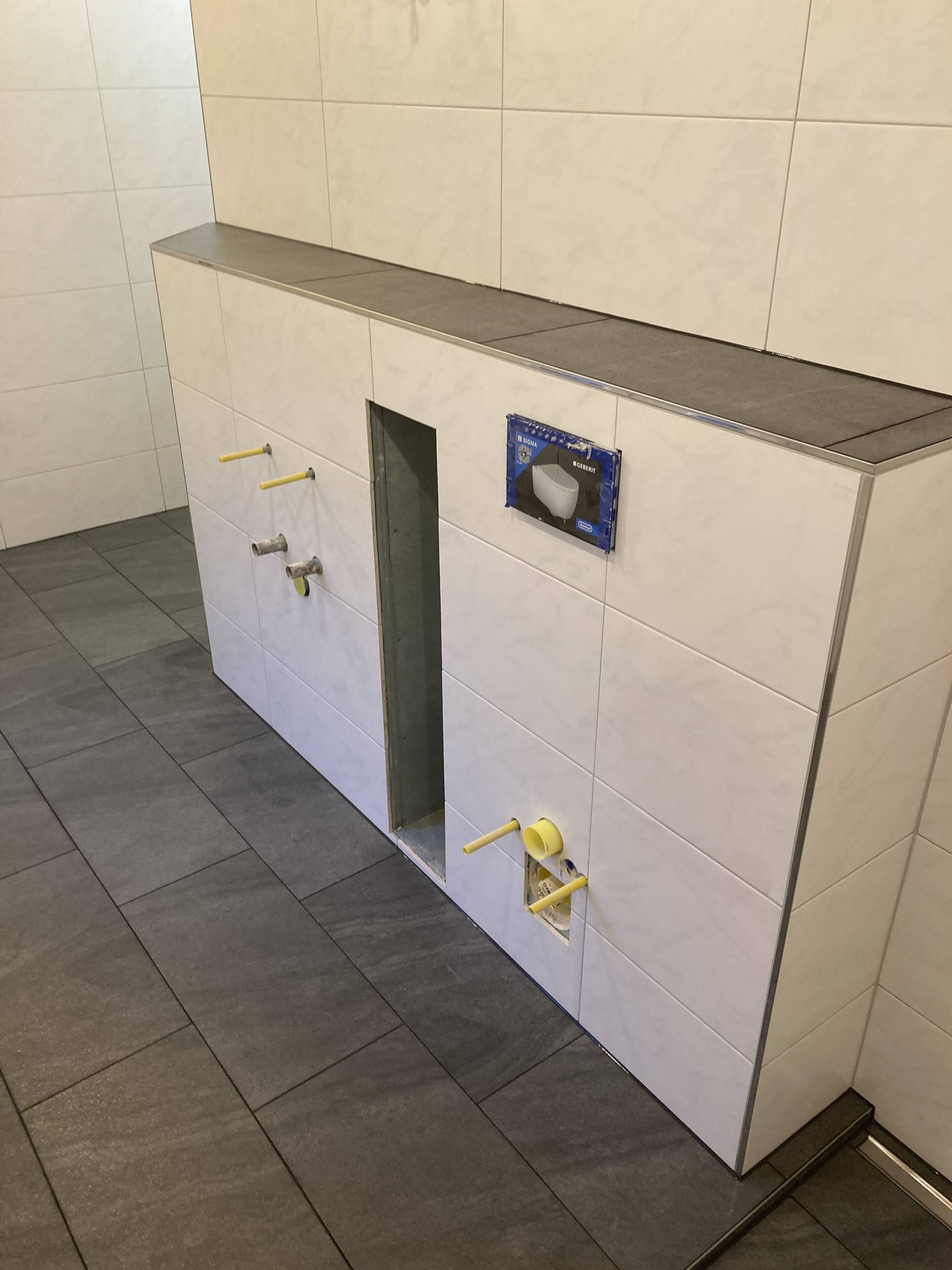 Badezimmerwand mit Sanitärarmaturen und einer Öffnung für eine Toilette, im Bau mit gefliesten Oberflächen.