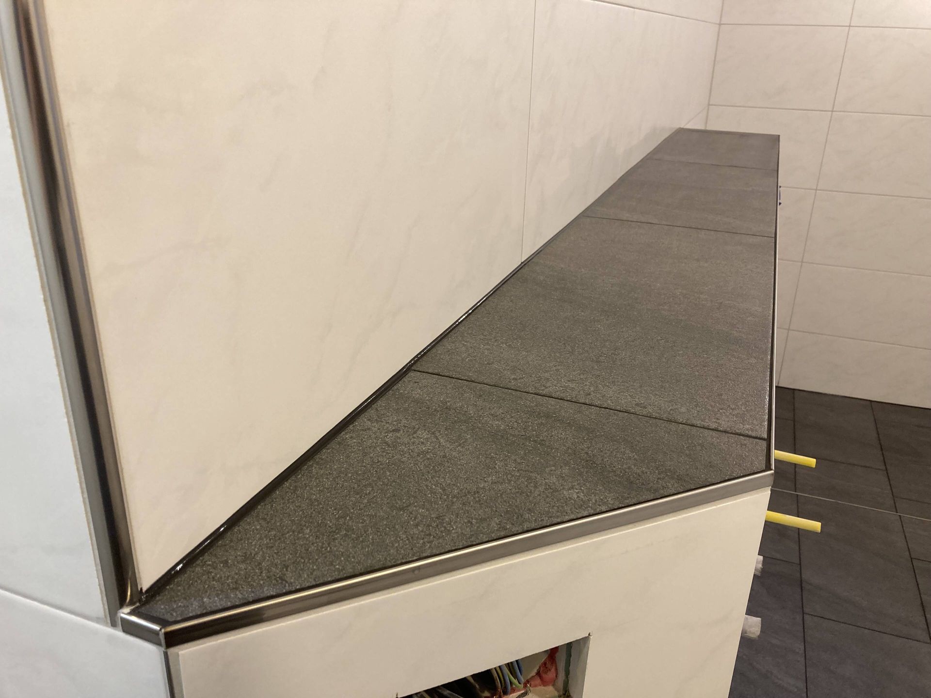 Grau geflieste Arbeitsplatte mit Metallkante vor weiß gefliester Wand.