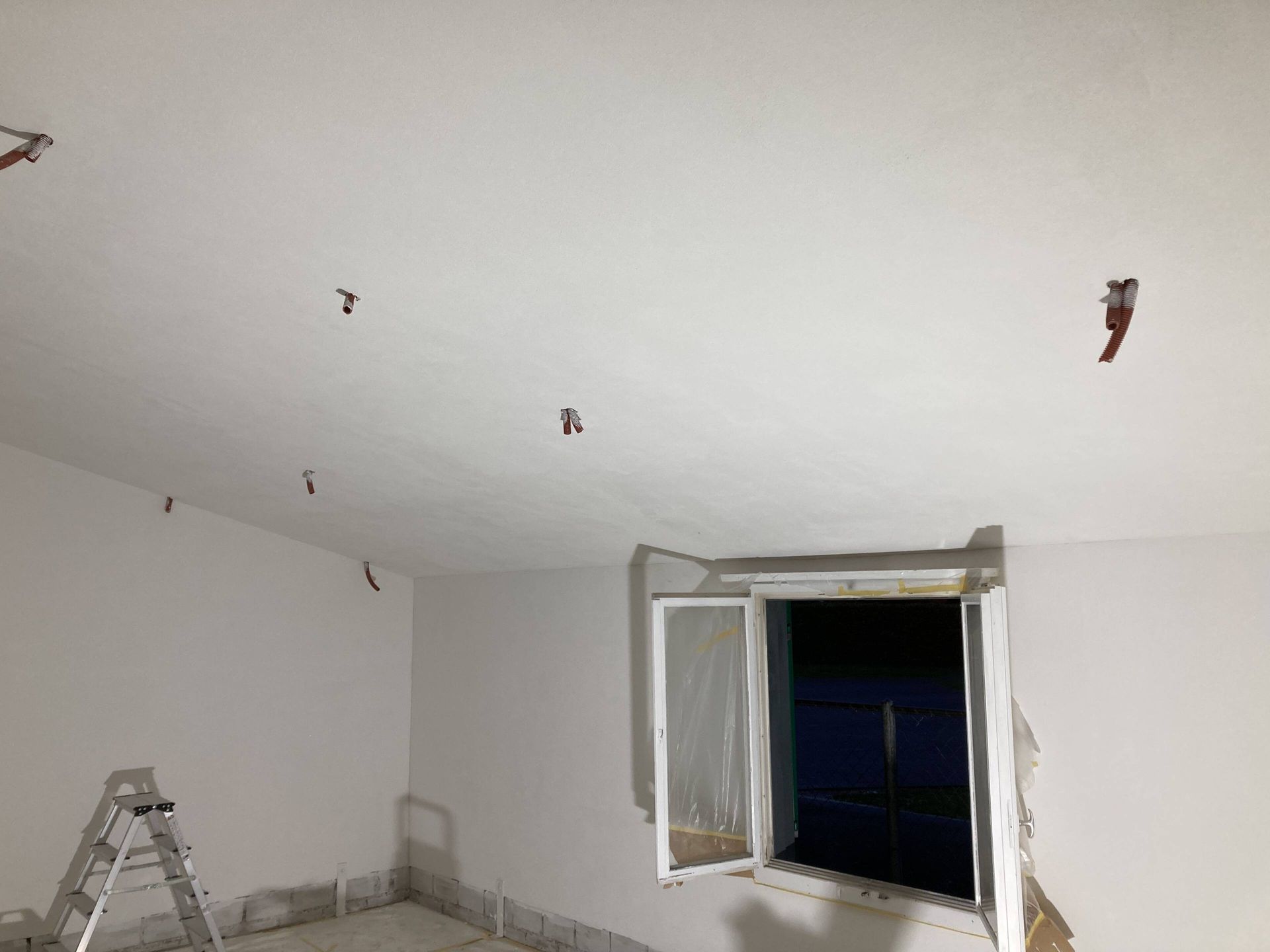 Weißer Raum mit Sprinklerköpfen an der Decke. Leiter links, offenes Fenster rechts.