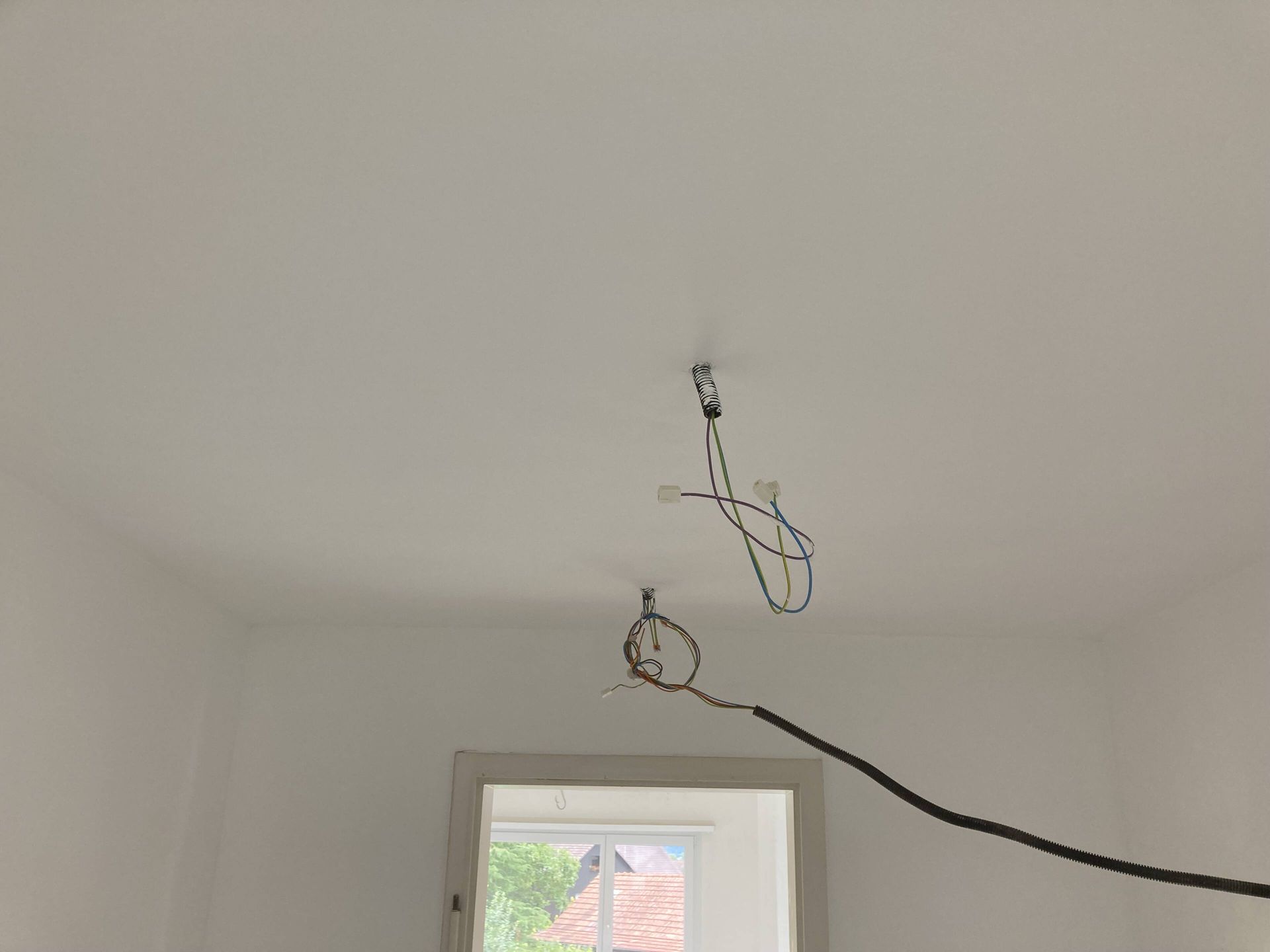 Weiße Zimmerdecke mit zwei baumelnden Stromkabeln, wahrscheinlich für die Beleuchtung.