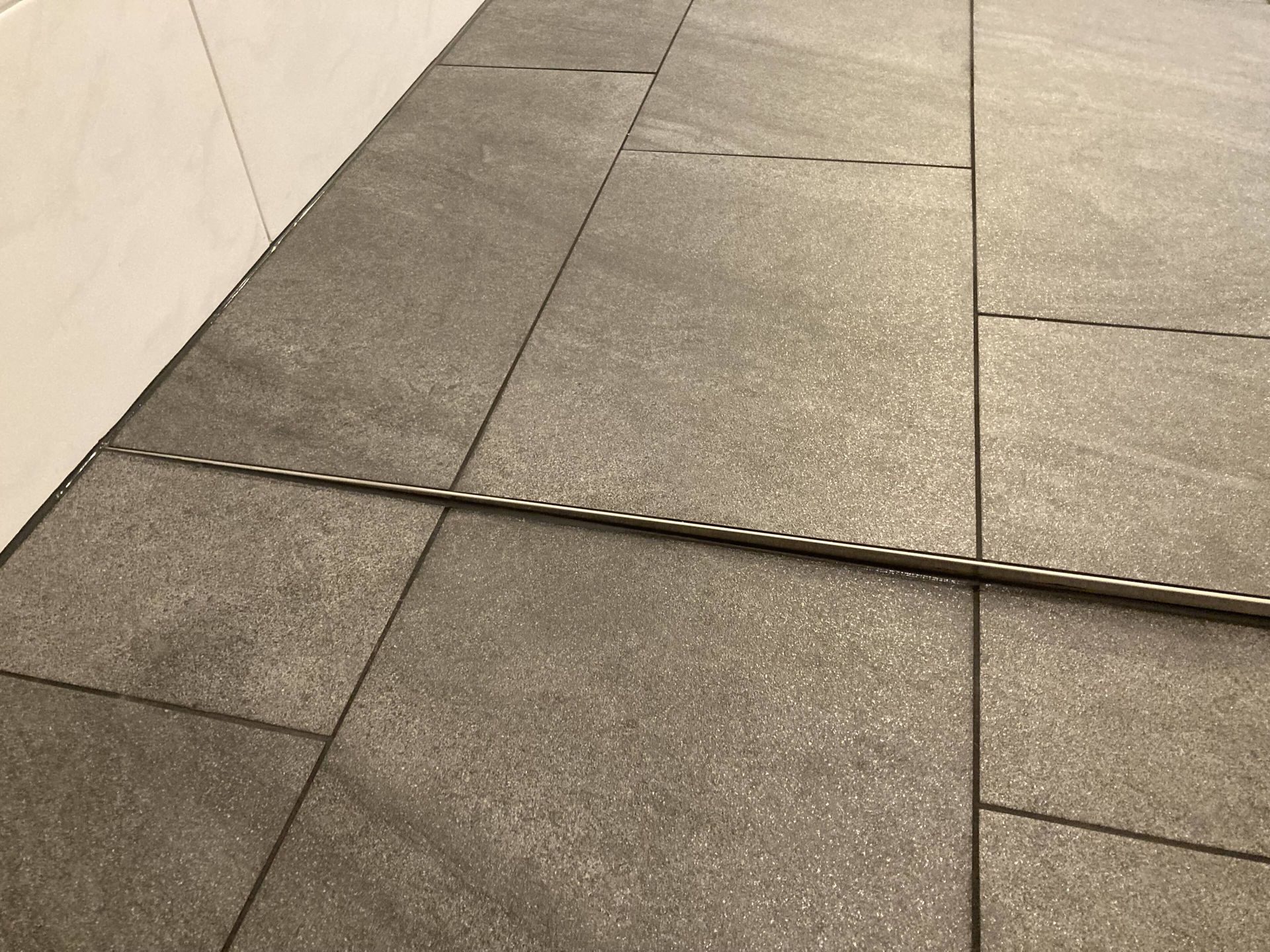 Grauer Fliesenboden mit einem Metallstreifen in der Mitte.