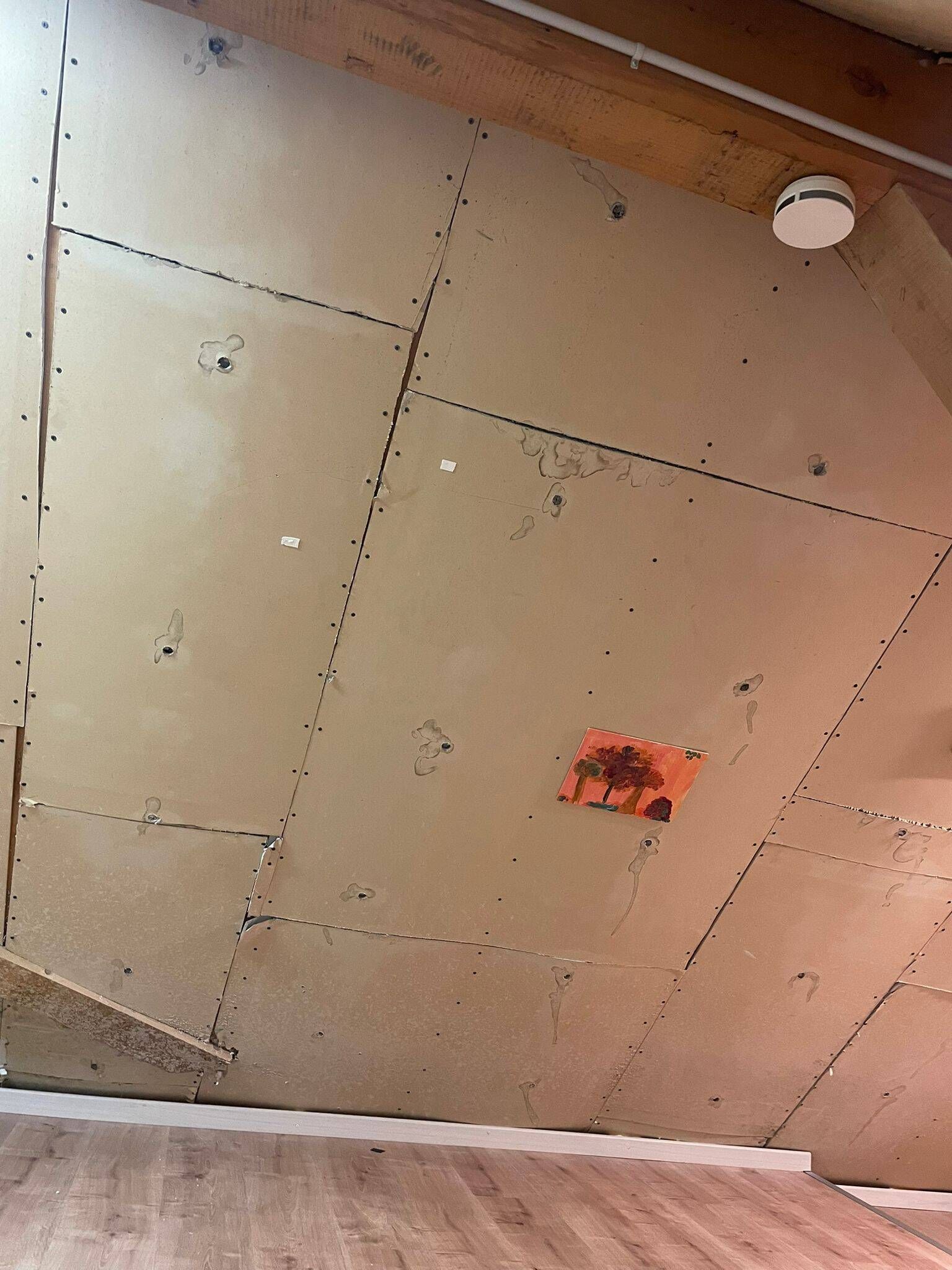 Hellbraune Wände mit sichtbaren Nähten und ein Rauchmelder in einem Raum mit Holzboden.