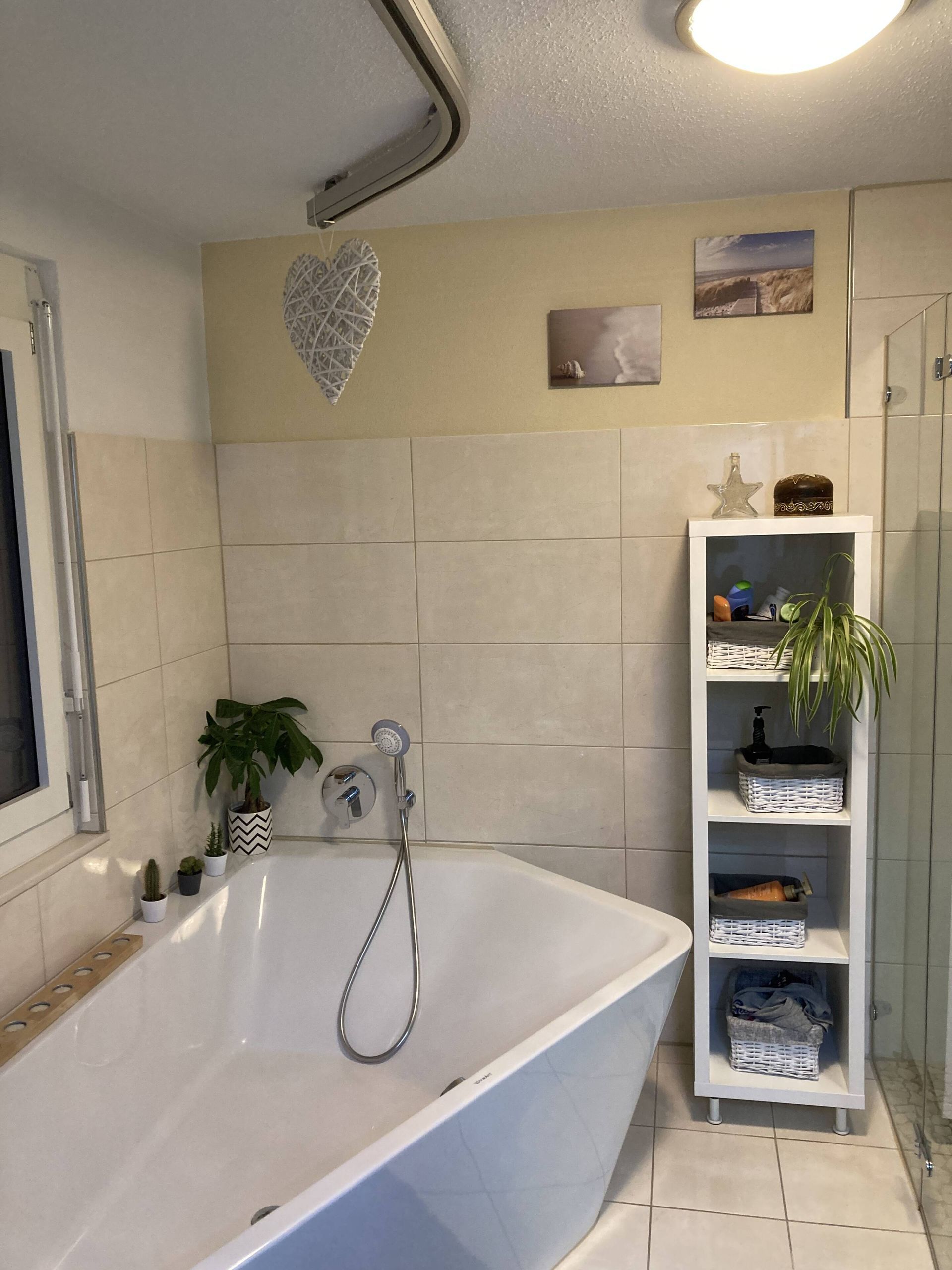 Badezimmer mit weißer Badewanne, weiß gefliesten Wänden und einem weißen Regal.