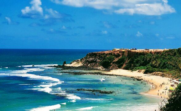 Vue panoramique d'une plage de sable fin et d'un littoral bordé par l'océan aux eaux turquoise sous un ciel dégagé.