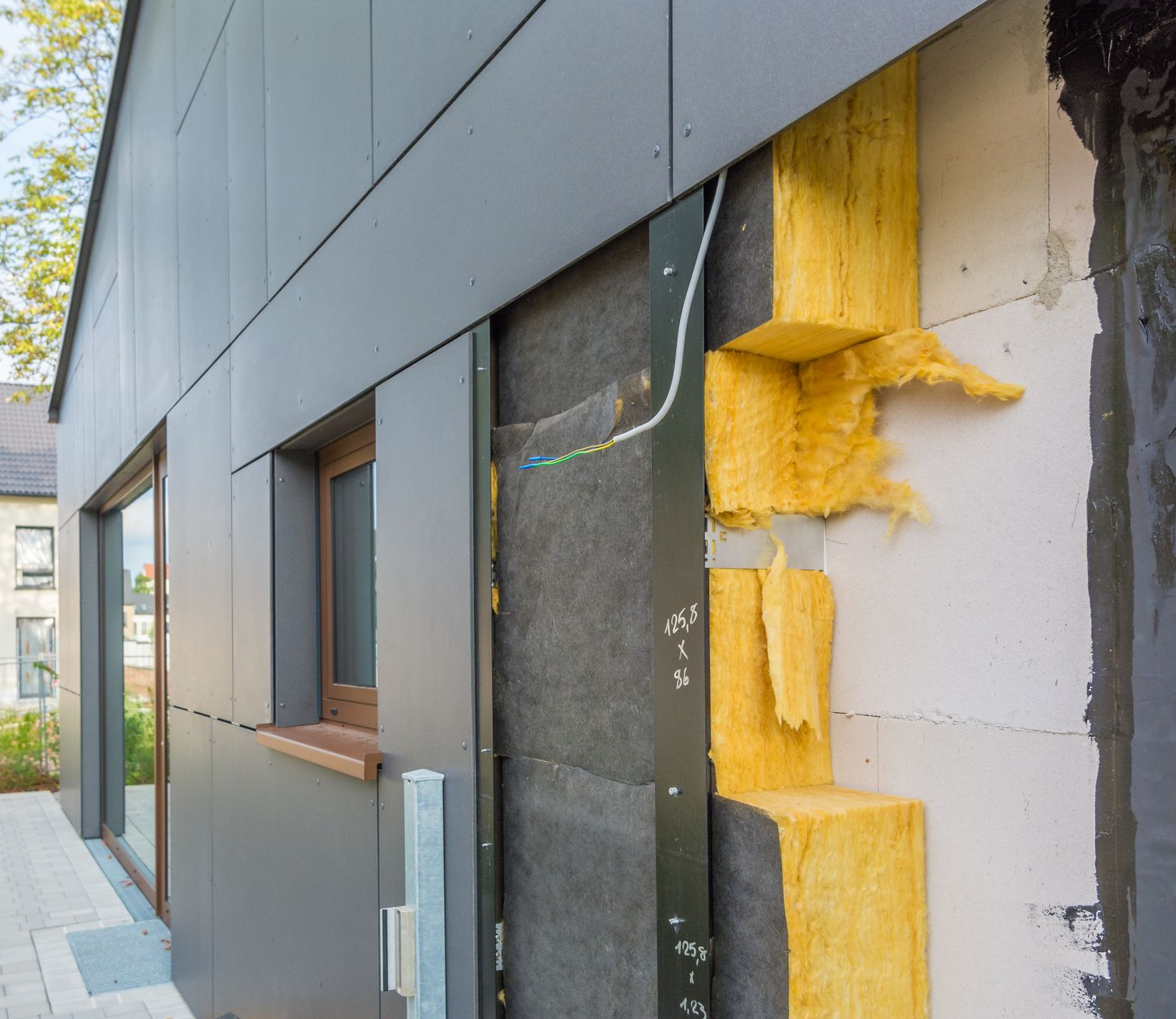 Isolation des murs extérieurs : revêtement métallique gris, isolation apparente, pare-vapeur noir, cadre de fenêtre en bois.