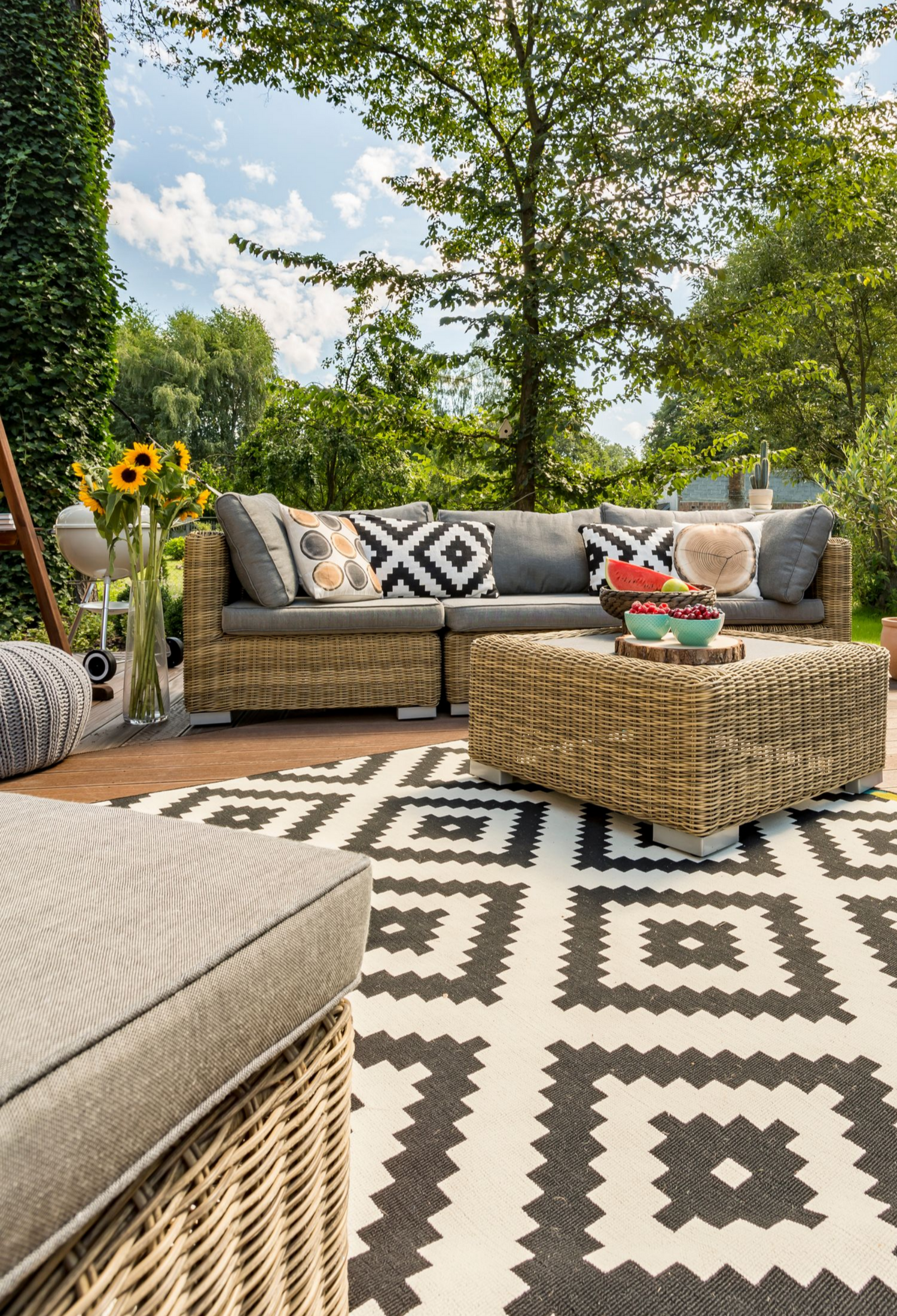 Terrasse extérieure avec mobilier en osier, tapis à motifs et verdure environnante.