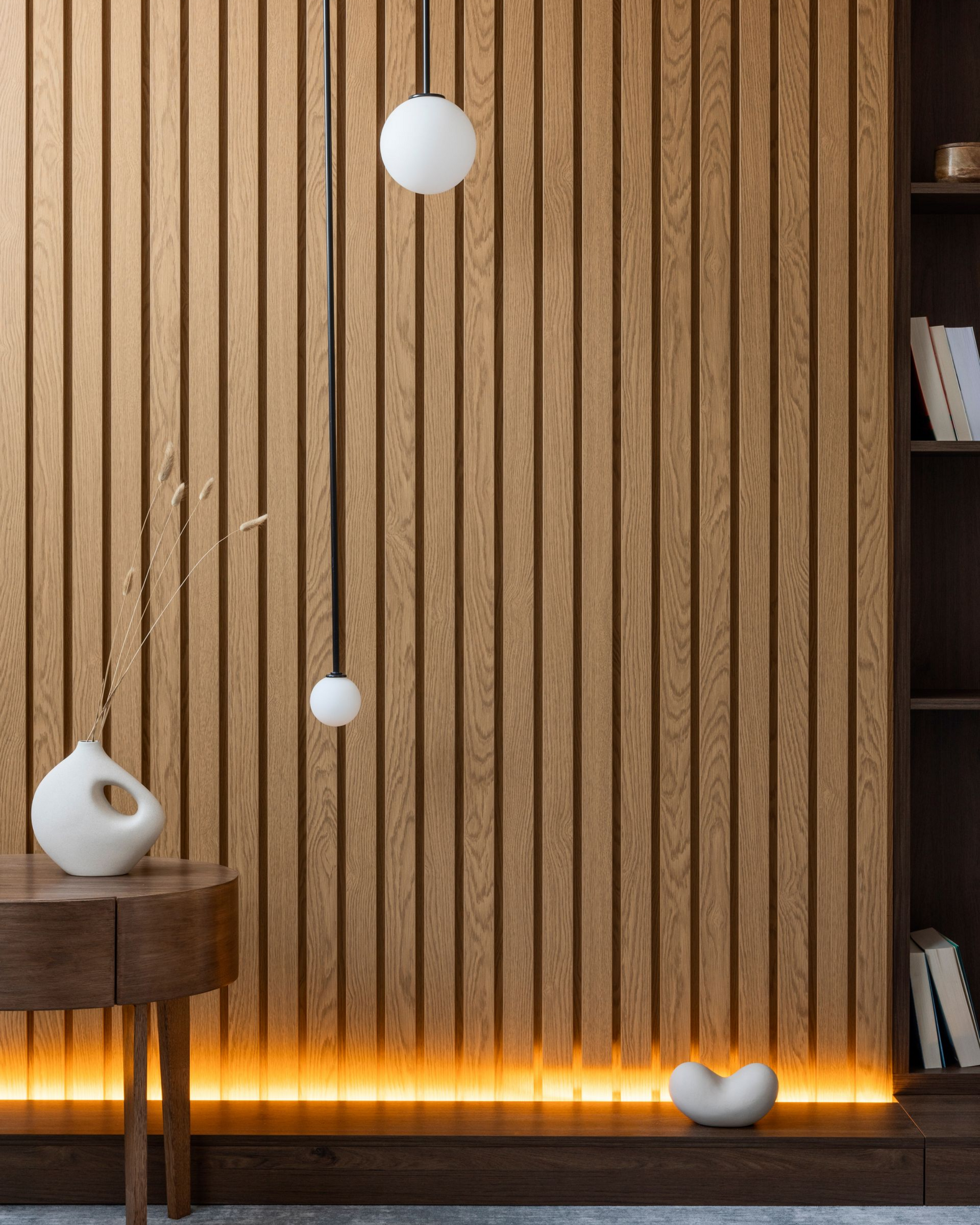 Mur en lattes de bois avec un luminaire suspendu, petite table d'appoint décorative et bibliothèque intégrée.