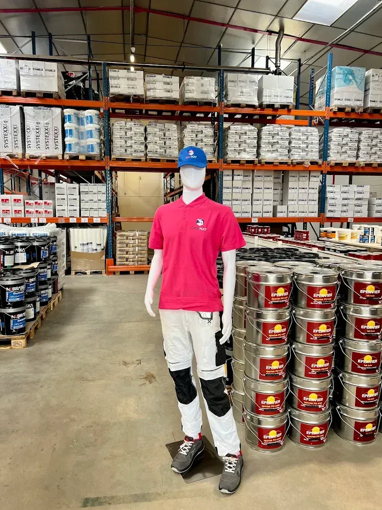 Un mannequin en tenue de travail se tient dans un entrepôt rempli de fournitures et de pots de peinture.