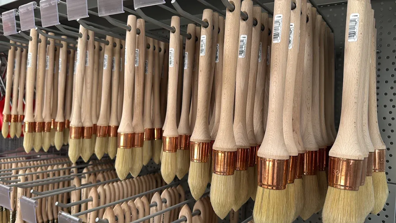 Des rangées de pinceaux suspendus à des supports métalliques, manches en bois, bagues en cuivre, poils clairs.