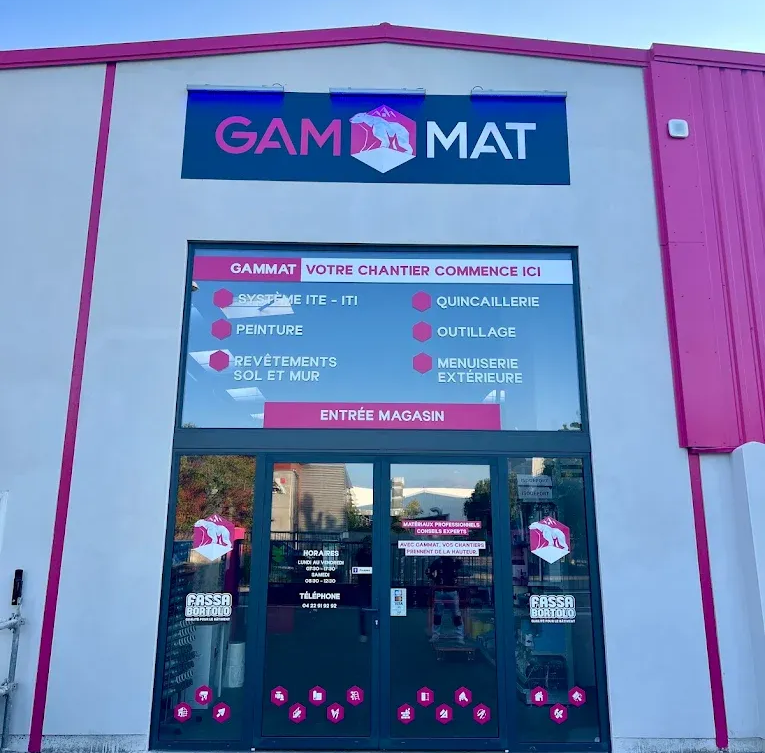 Extérieur du magasin GAMMAT avec enseigne rose et noire, portes d'entrée et listes de produits.