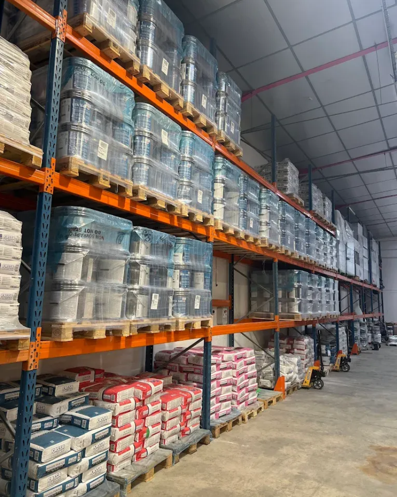 Des étagères d'entrepôt remplies de palettes de marchandises emballées et de sacs de matériaux de construction.