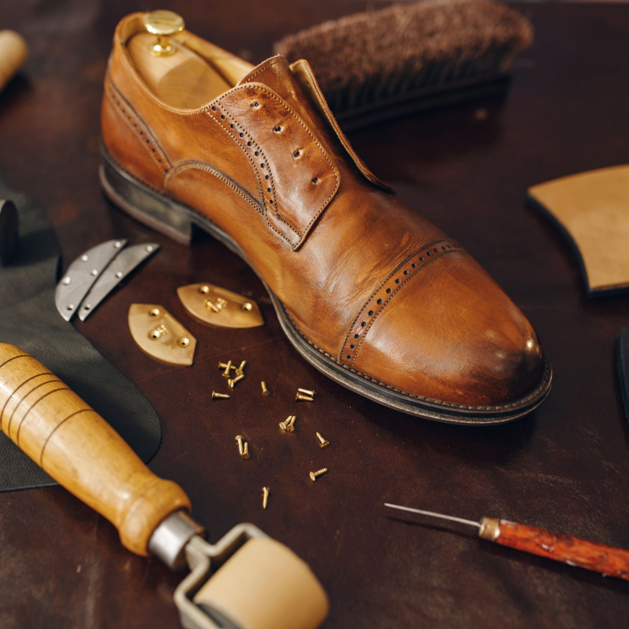 Chaussure en cuir en cours de fabrication, entourée d'outils de cordonnerie.