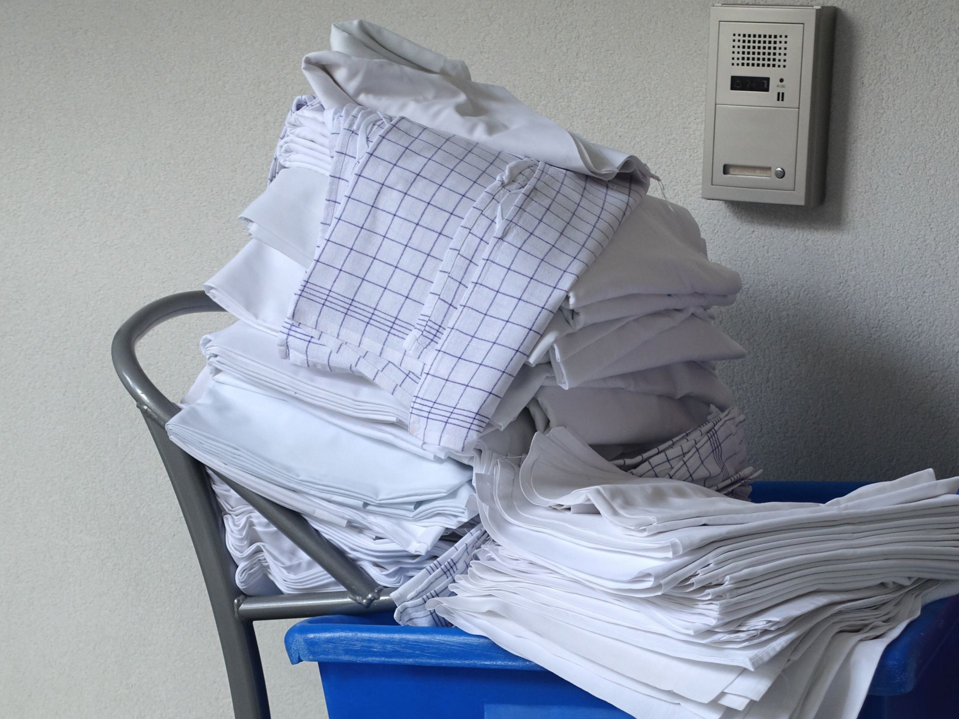 Un tas de tissu blanc plié dans un bac bleu sur un chariot métallique.