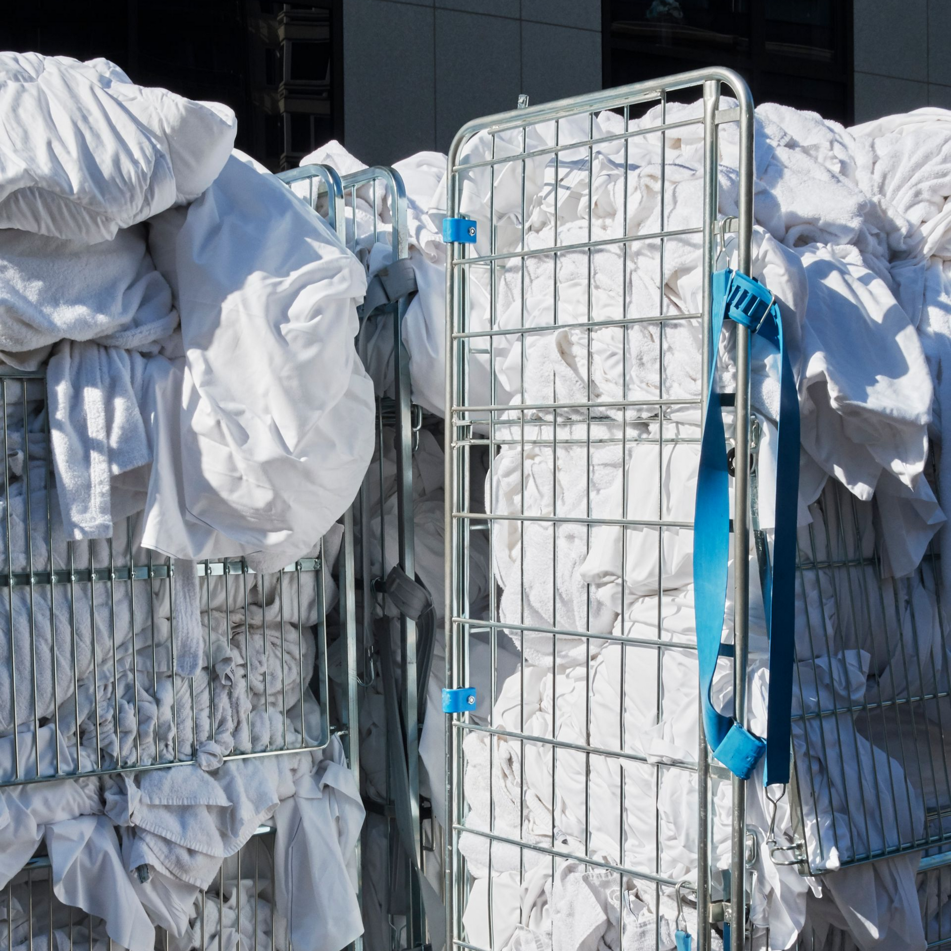 Du linge blanc empilé dans des chariots à linge en métal.