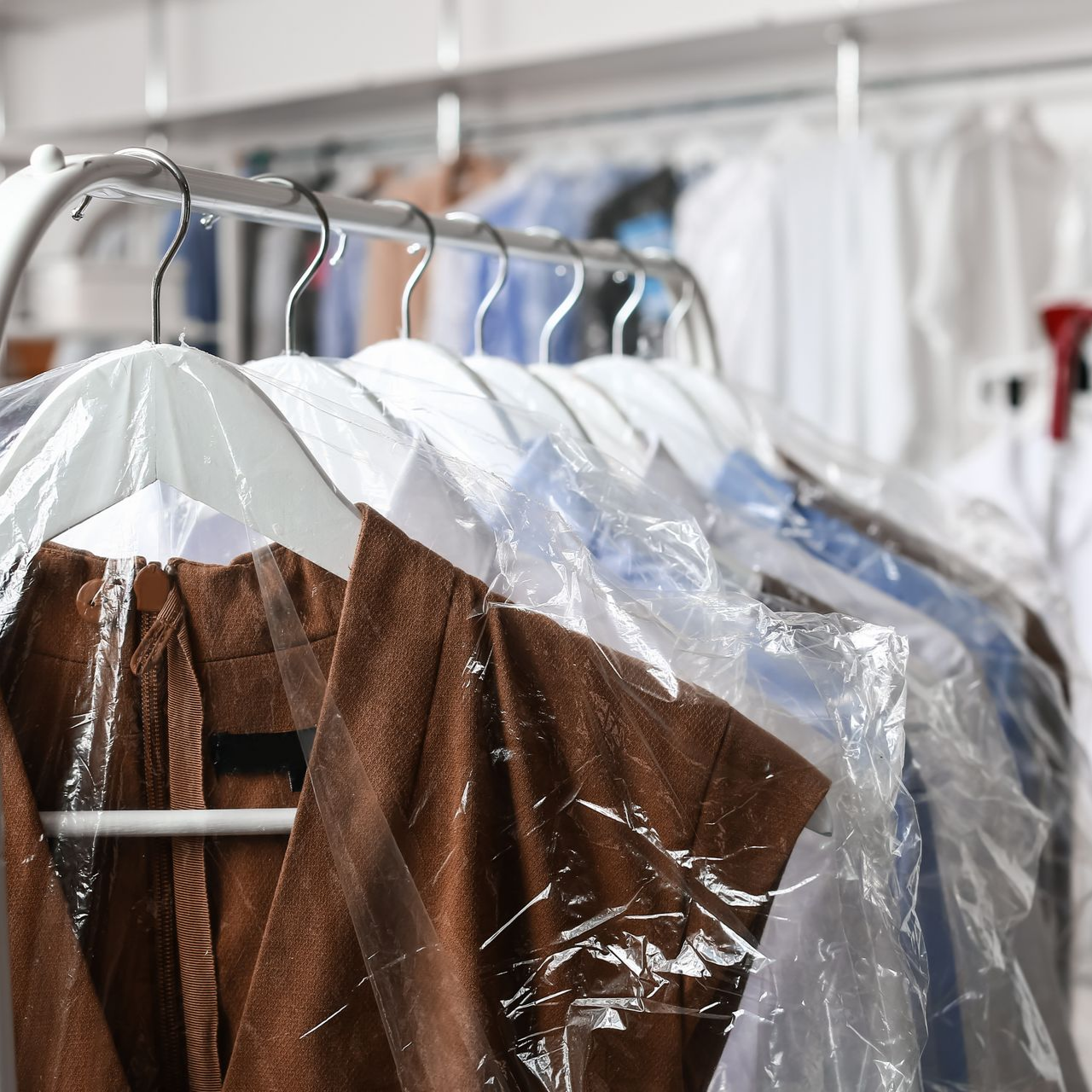 Des vêtements sur des cintres recouverts de plastique dans un pressing.