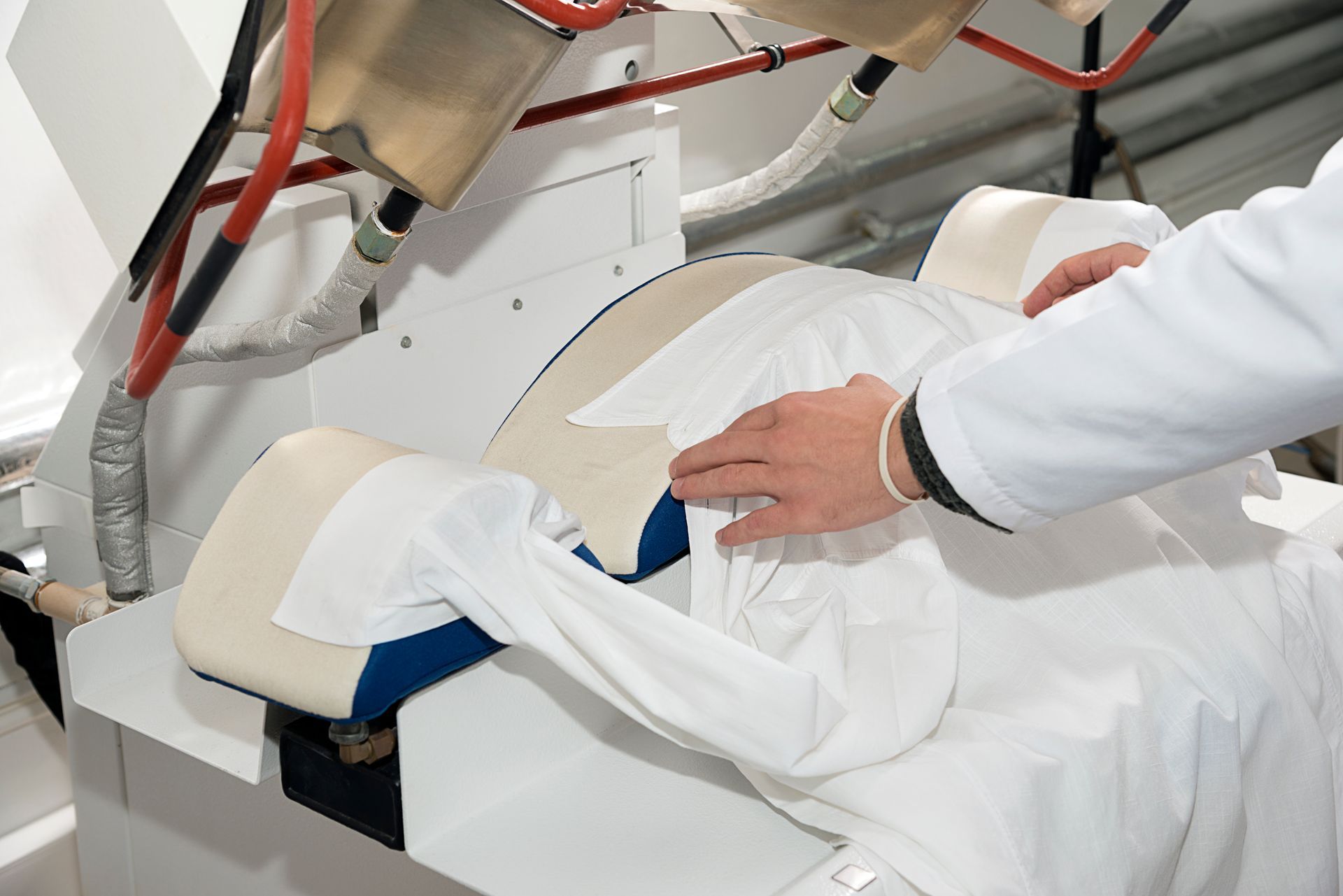 Une personne en blouse blanche utilise une presse à chemises industrielle.