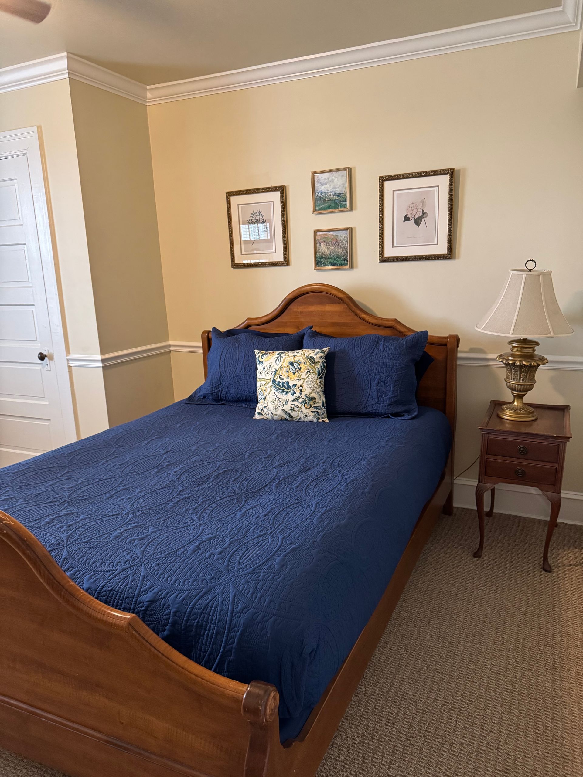 A bedroom with a bed , nightstand , lamp and pictures on the wall.