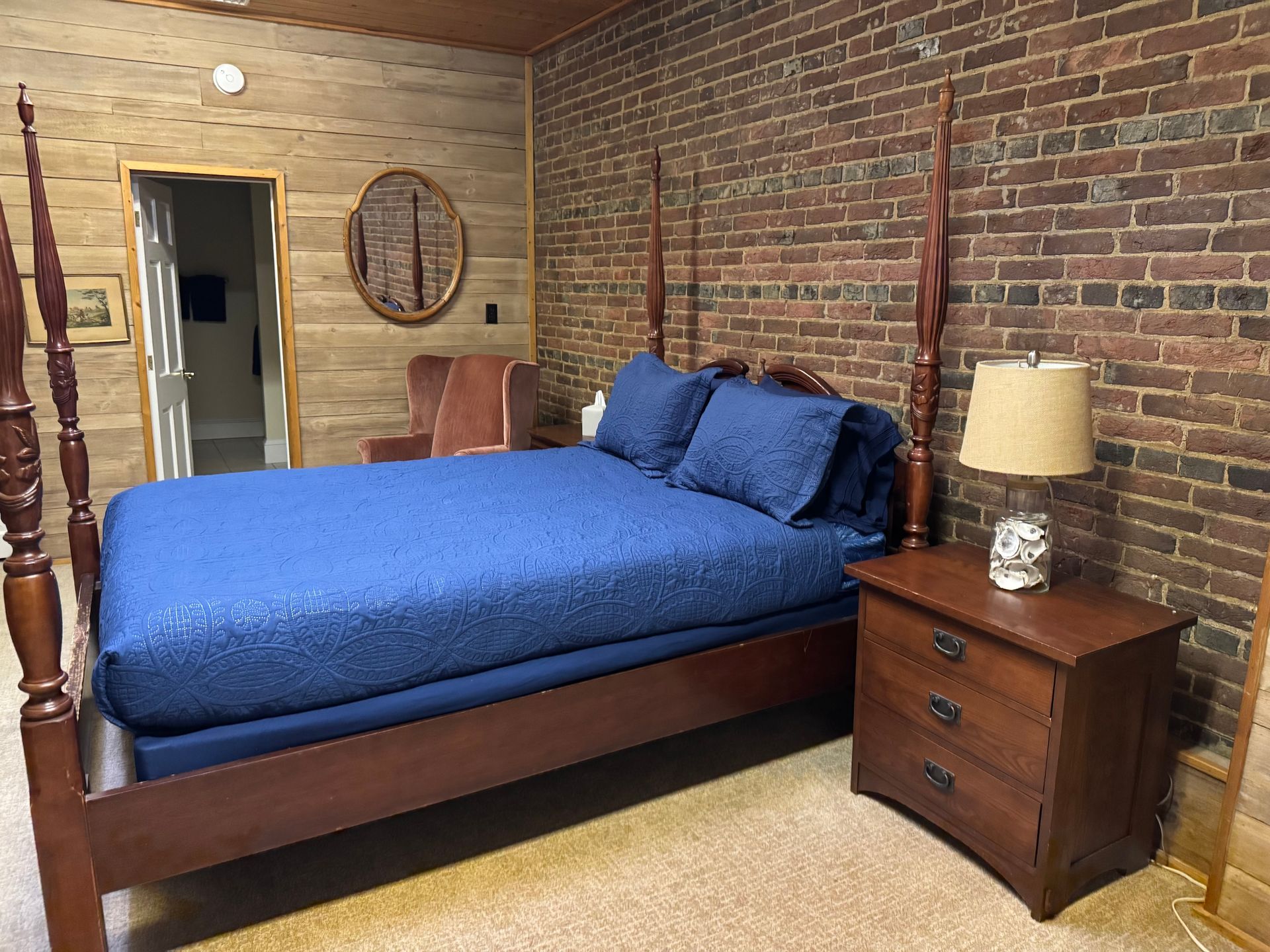A bedroom with a bed , nightstand , lamp and brick wall.