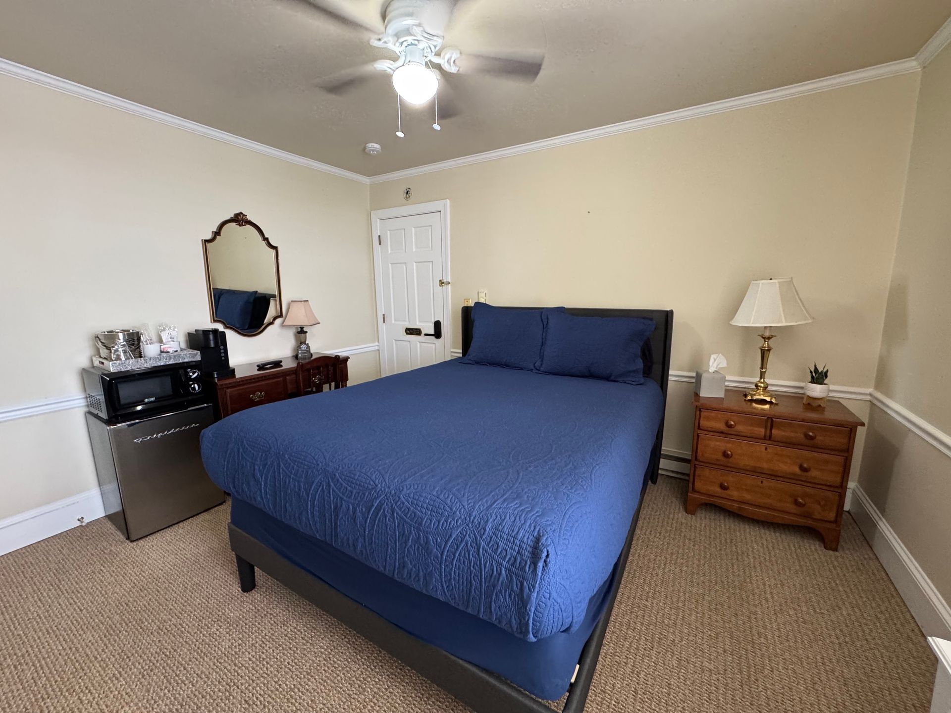 A bedroom with a bed , nightstand , microwave and ceiling fan.
