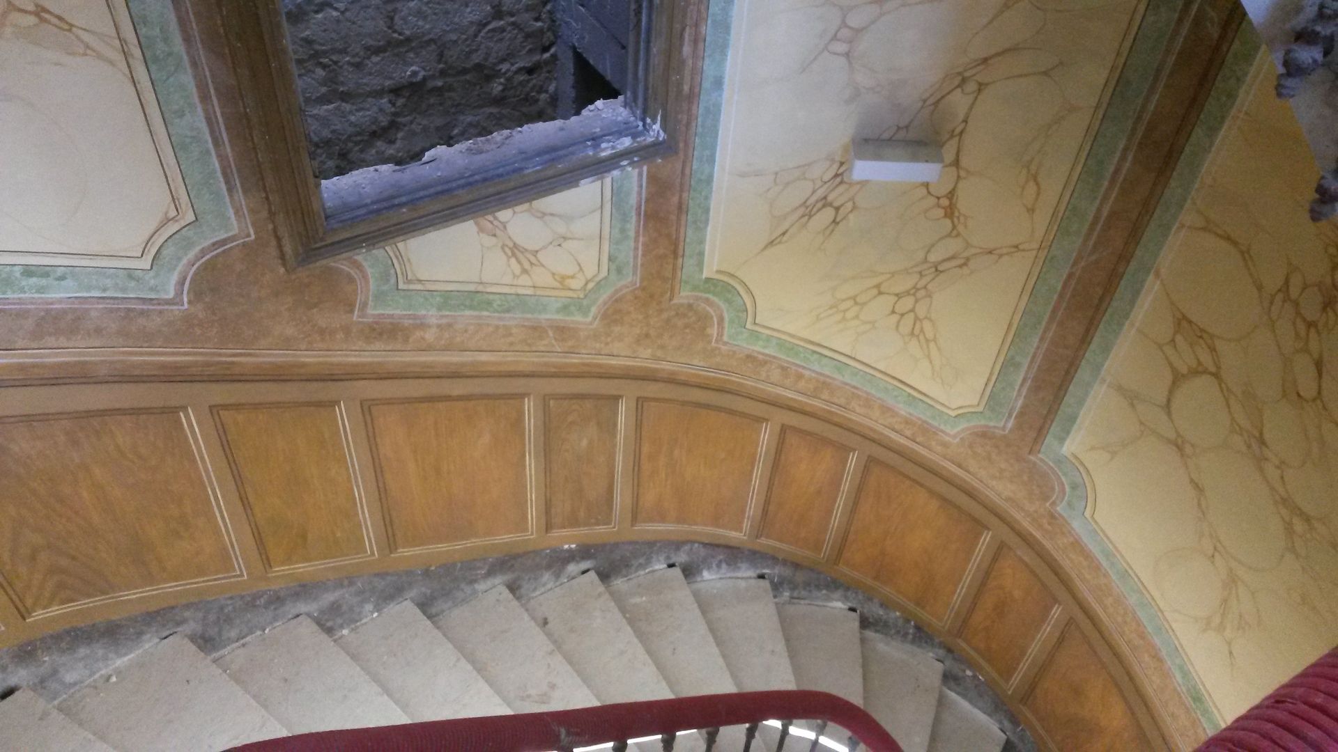 Un escalier en colimaçon avec une rampe rouge et une fenêtre.