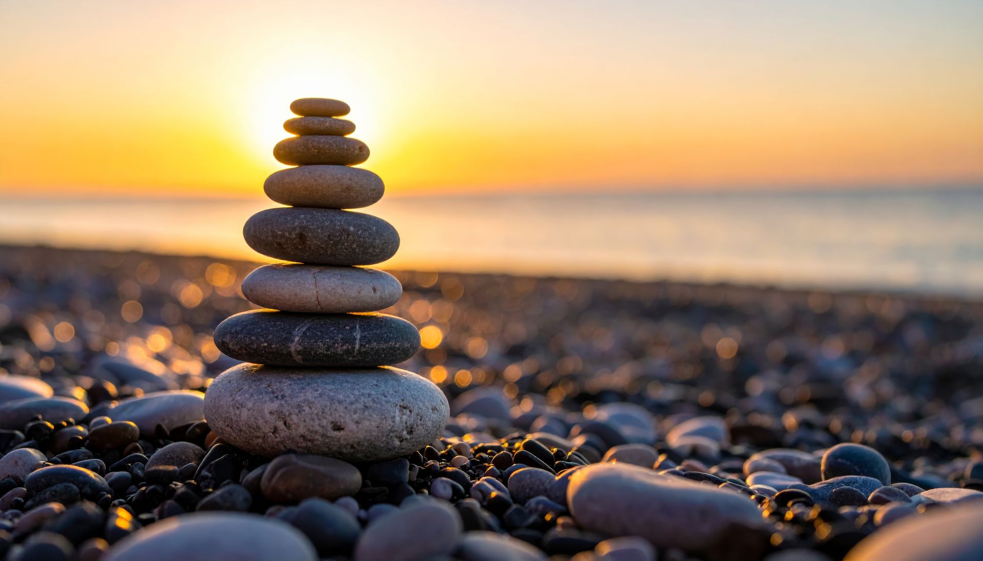 Des pierres empilées sur une plage, avec un coucher de soleil orangé sur l'océan en arrière-plan.