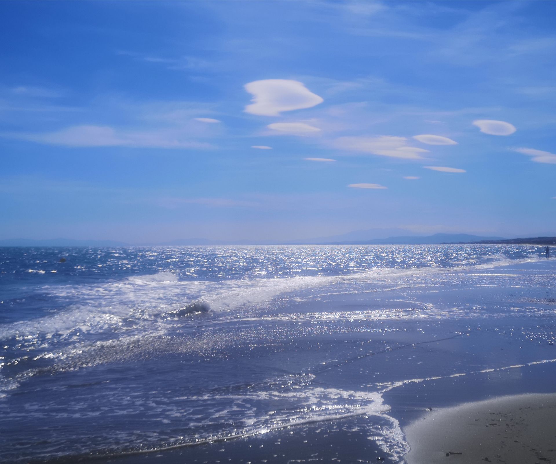 Soleil éclatant sur les vagues de l'océan, ciel bleu parsemé de petits nuages.