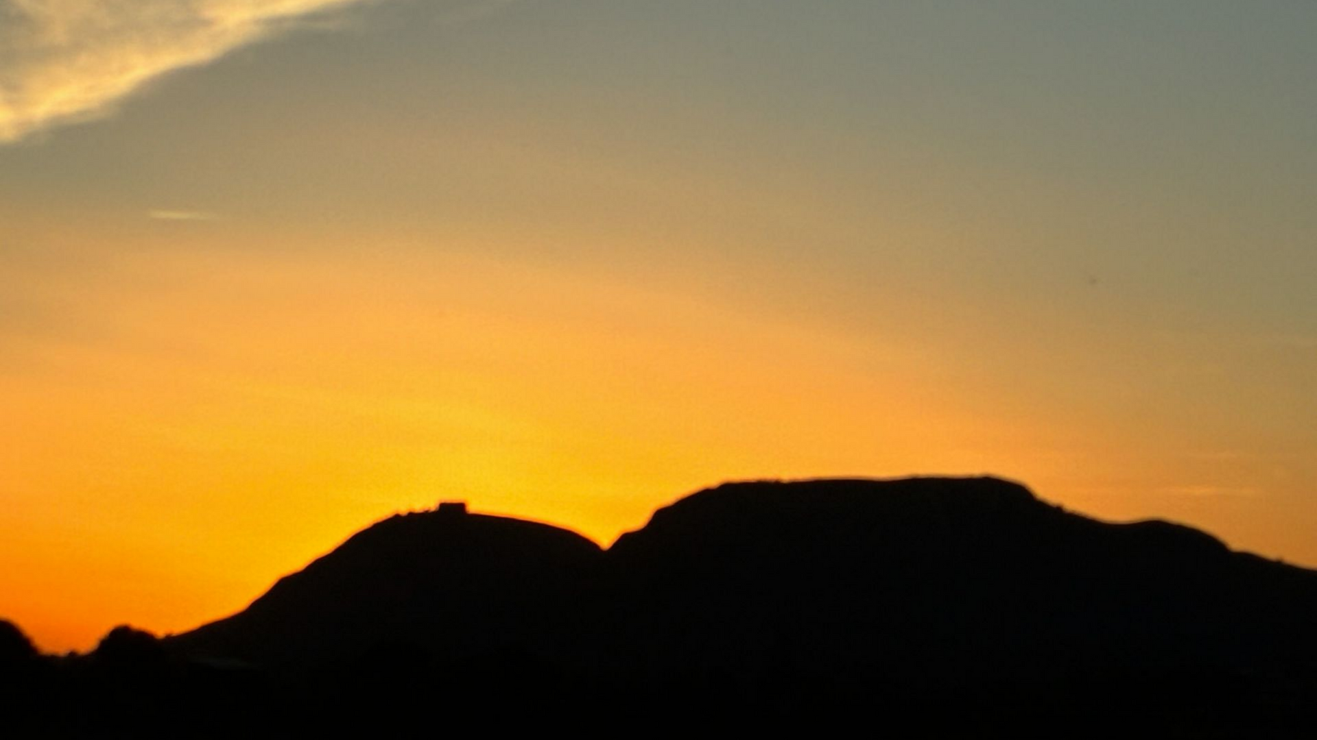 Montagnes en silhouette sur un coucher de soleil doré, orangé et bleu.