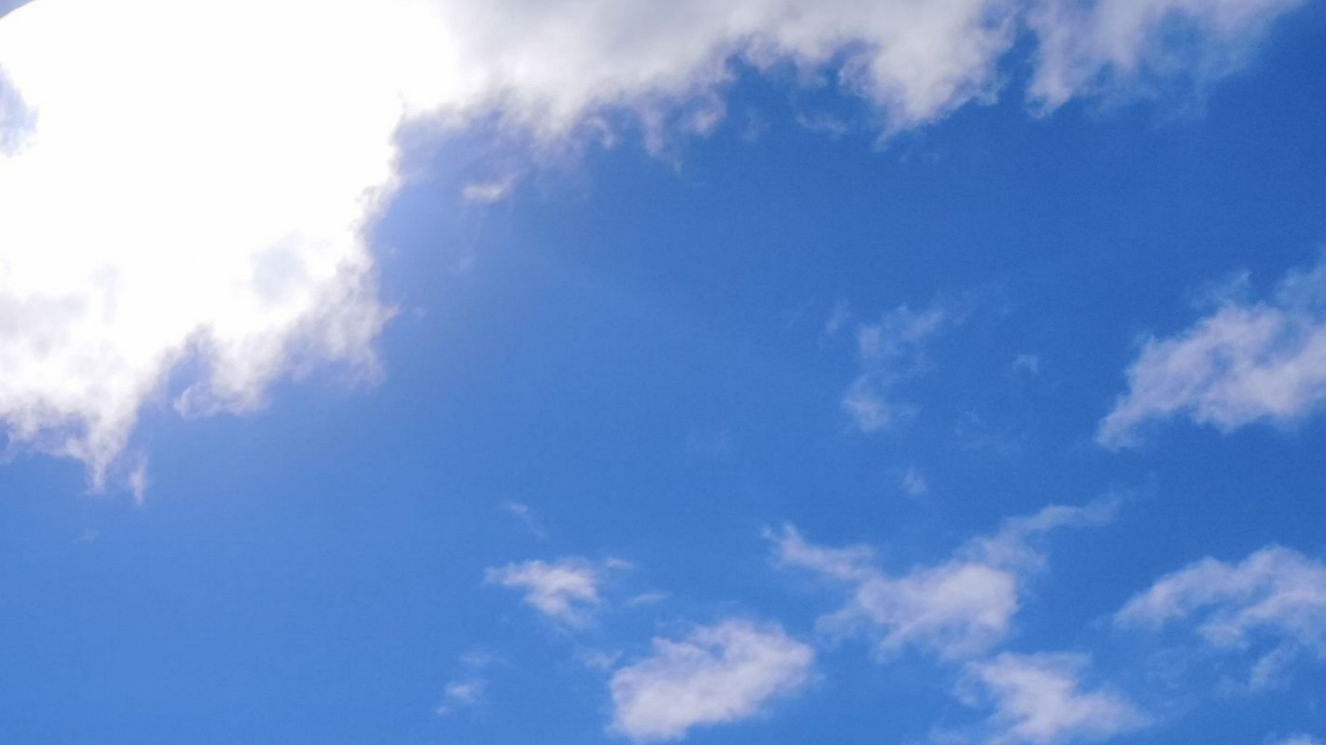 Ciel bleu éclatant parsemé de nuages ​​blancs, laissant filtrer la lumière du soleil.