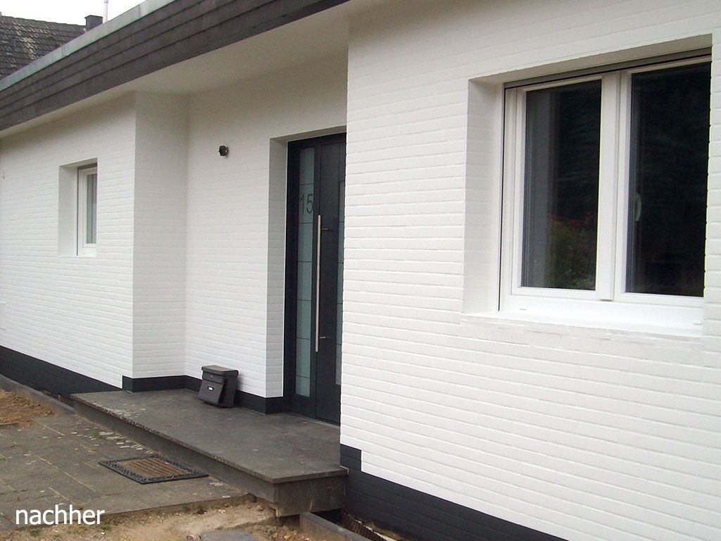 Ein weißes Backsteinhaus mit einer schwarzen Tür und Fenstern