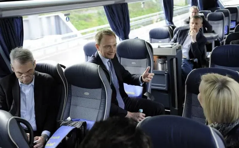 Eine Gruppe von Menschen sitzt in einem Bus und unterhält sich, darunter Christian Lindner, 02elf Travel GmbH & Co KG
