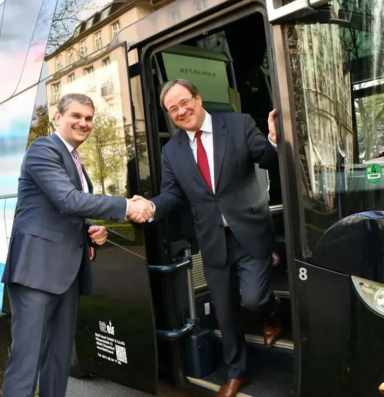 Zwei Männer schütteln sich vor einem Bus mit der Nummer 8 die Hände, 02elf Travel GmbH & Co KG