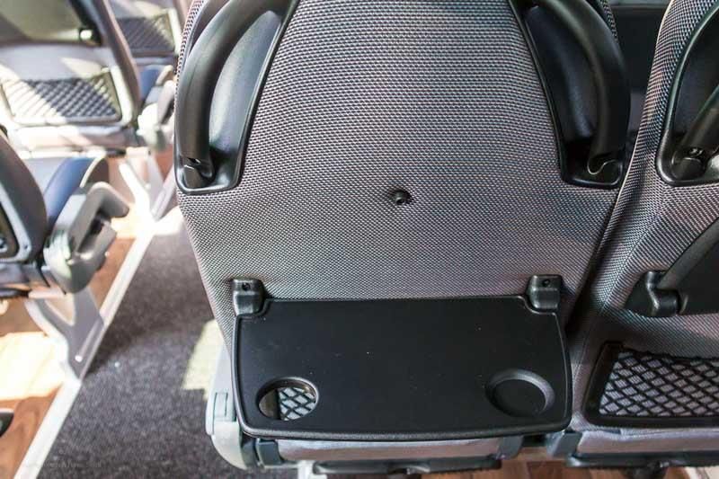 Rückenlehne eines Zugsitzes mit ausklappbarem Tisch und Getränkehalter, abgebildet im Inneren eines Waggons.