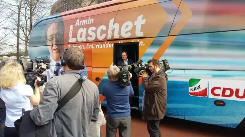 Eine Gruppe von Menschen steht vor einem Bus mit der Aufschrift „Armin Laschet“, 02elf Travel GmbH & Co KG