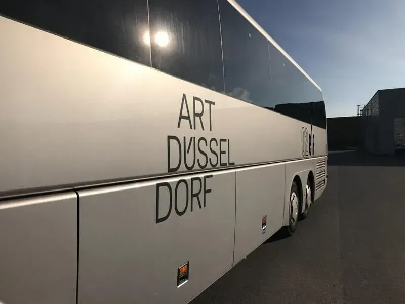 Ein weißer Bus mit der Aufschrift „Art Düsseldorf“ an der Seite, 02elf Travel GmbH & Co KG