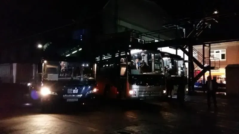 Zwei Busse parken nachts vor einem Gebäude.