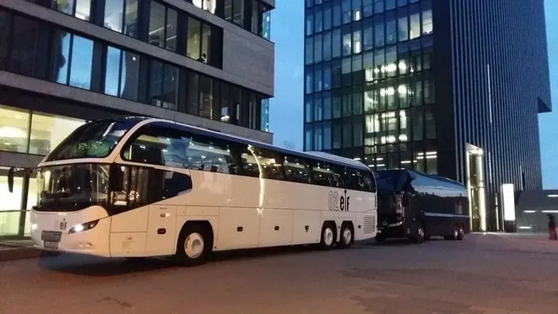 Ein weißer Bus parkt vor einem hohen Gebäude. 02elf Travel GmbH & Co KG